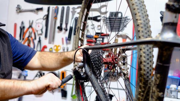 A bike is hanging on a work stand. A person is adjusting the derailleur