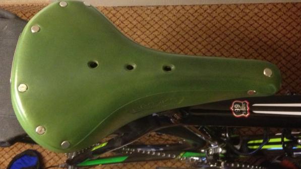 A close-up of a green Brooks saddle on a black bike, taken from above