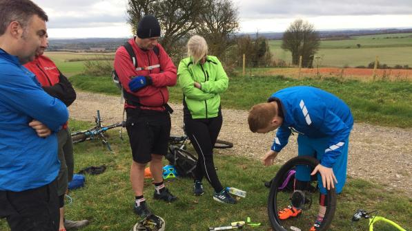 Four people are watching a man removing a tyre from a bike wheel