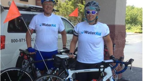A man and a woman stand behind their bikes. They're wearing WaterAid t-shirts and helmets