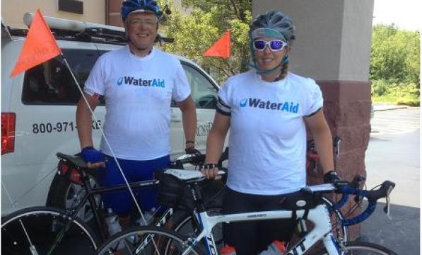 A man and a woman stand behind their bikes. They're wearing WaterAid t-shirts and helmets