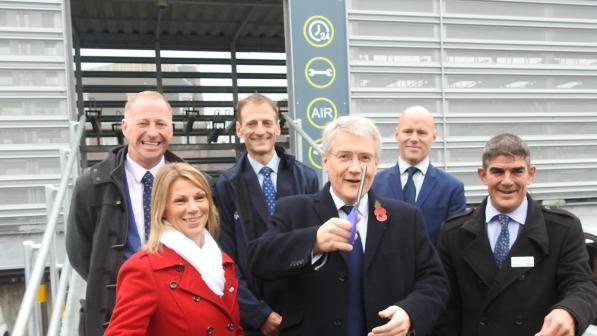 A group of people are standing in front a building with a Cycle Hub sign above the door. A man at the front is cutting a red ribbon