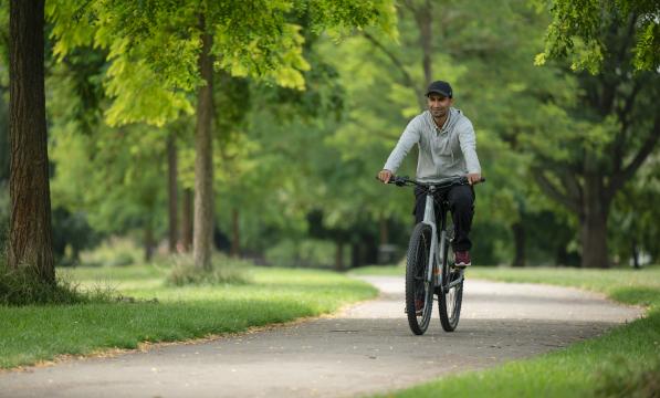 A man wearing a grey cap pedals an e-cycle through a park on a sunny day