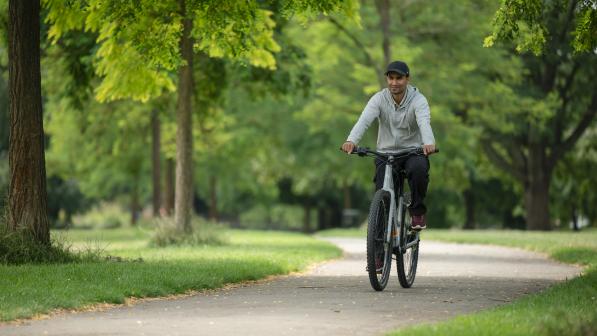 A man wearing a grey cap pedals an e-cycle through a park on a sunny day